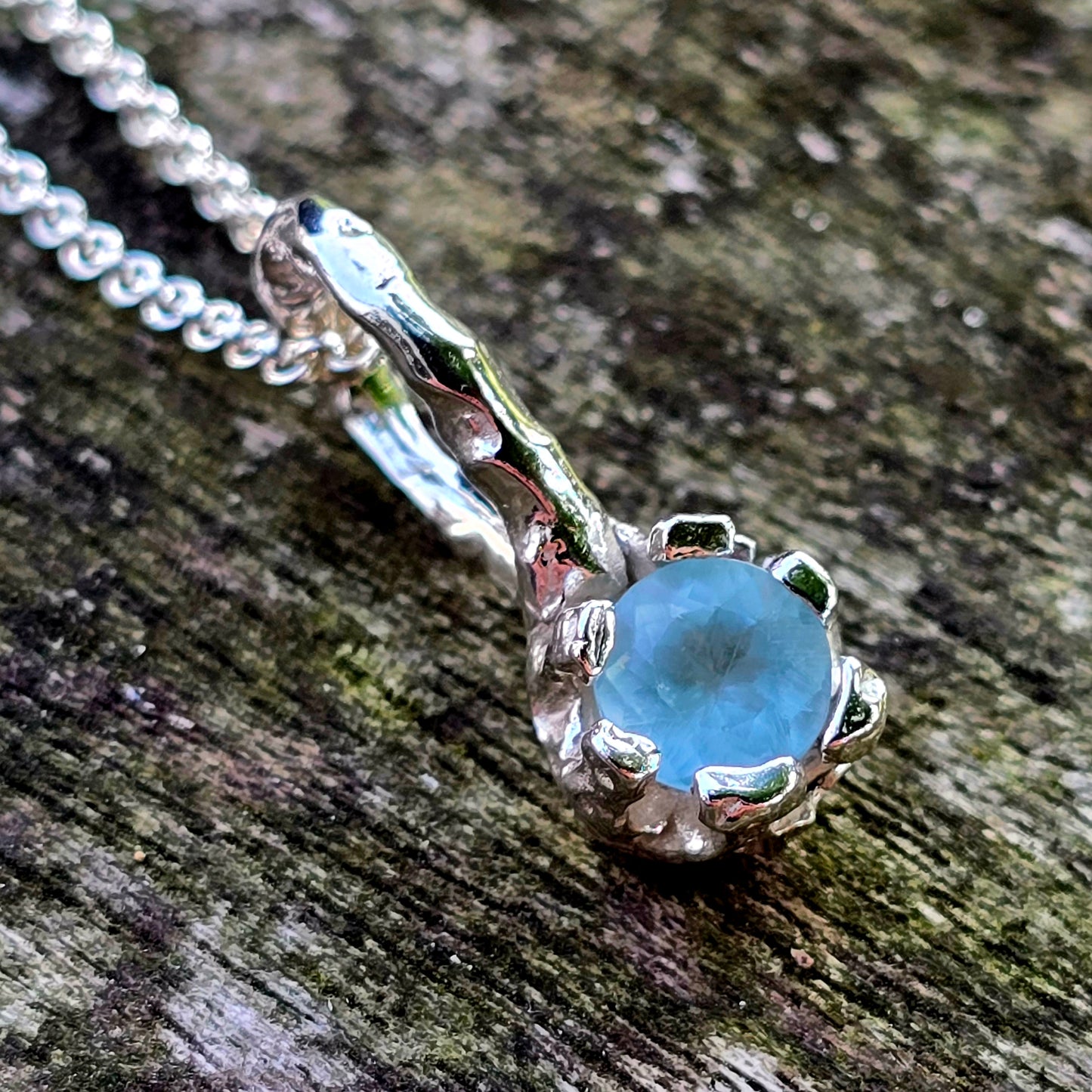 Handgefertigter Silberanhänger mit rundem, facettierten Apatit in Krallenfassung. Der Anhänger erinnert an einen zarten Ast oder eine Wurzel, die den leuchtend blauen Edelstein hält – organisches Design, inspiriert von der Natur. Ideal als einzigartiges Schmuckstück für Naturliebhaberinnen.