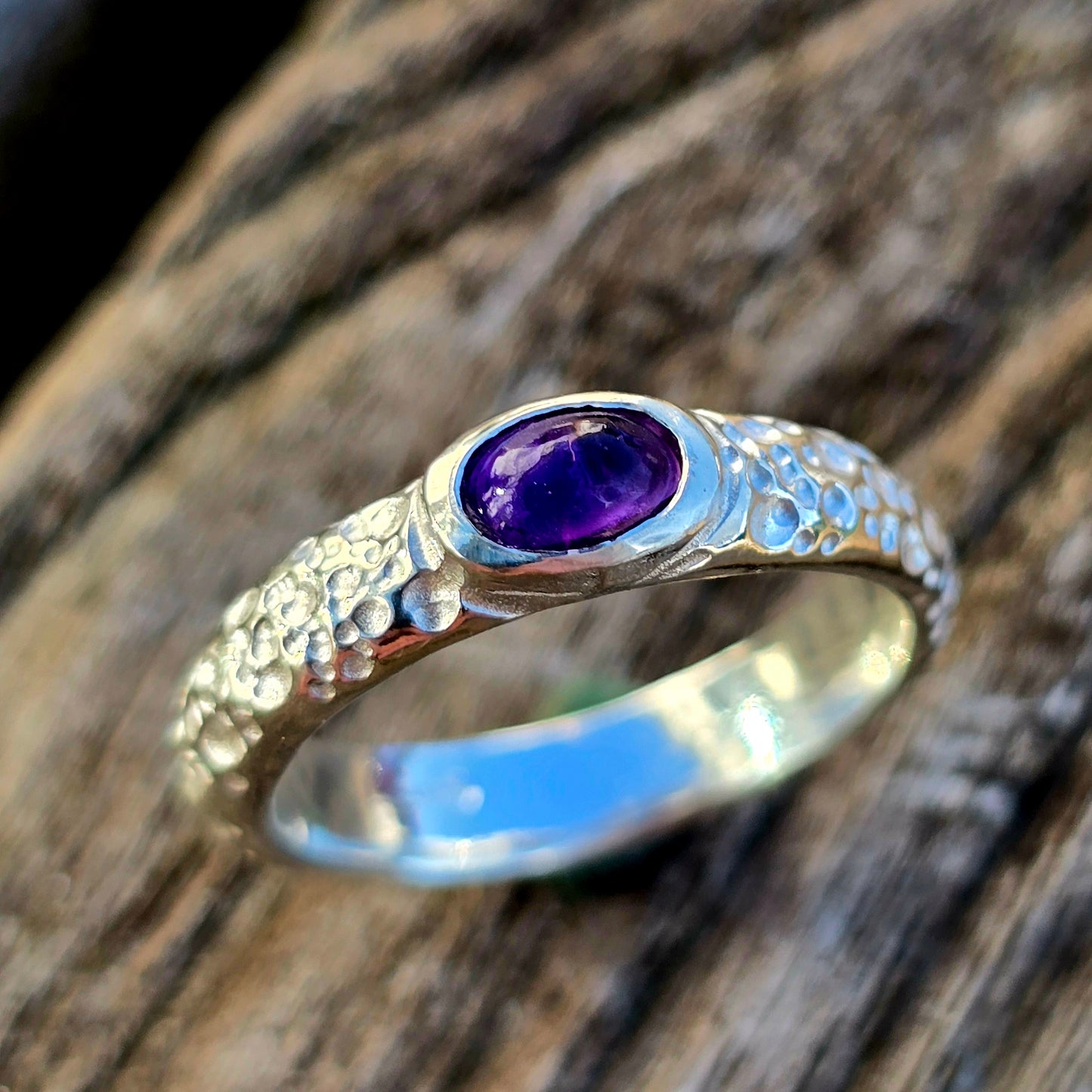 Handgefertigter Silberring mit einem tiefvioletten Amethyst-Cabochon, verziert mit einer strukturierten, organischen Oberfläche. Ein einzigartiges Schmuckstück aus dem Lost-Wax-Verfahren, präsentiert auf rustikalem Holz