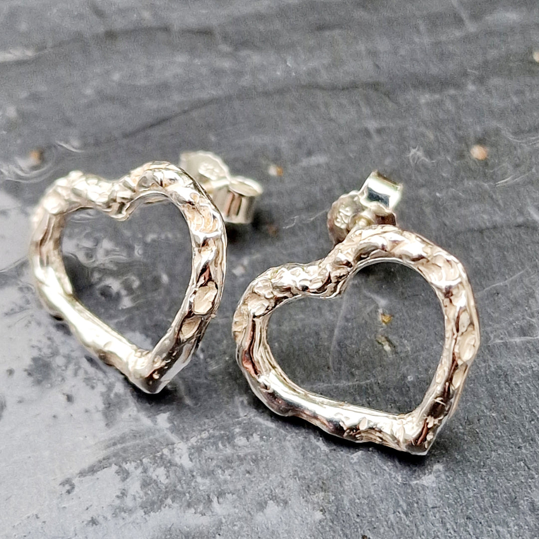 Handgefertigte Herz-Ohrstecker aus Silber mit organischer, gehämmerter Struktur. Die offenen Herzformen verleihen den Ohrringen eine filigrane, moderne Ästhetik. Perfekter Silberschmuck für Liebhaber von einzigartigem, natürlichem Design.
