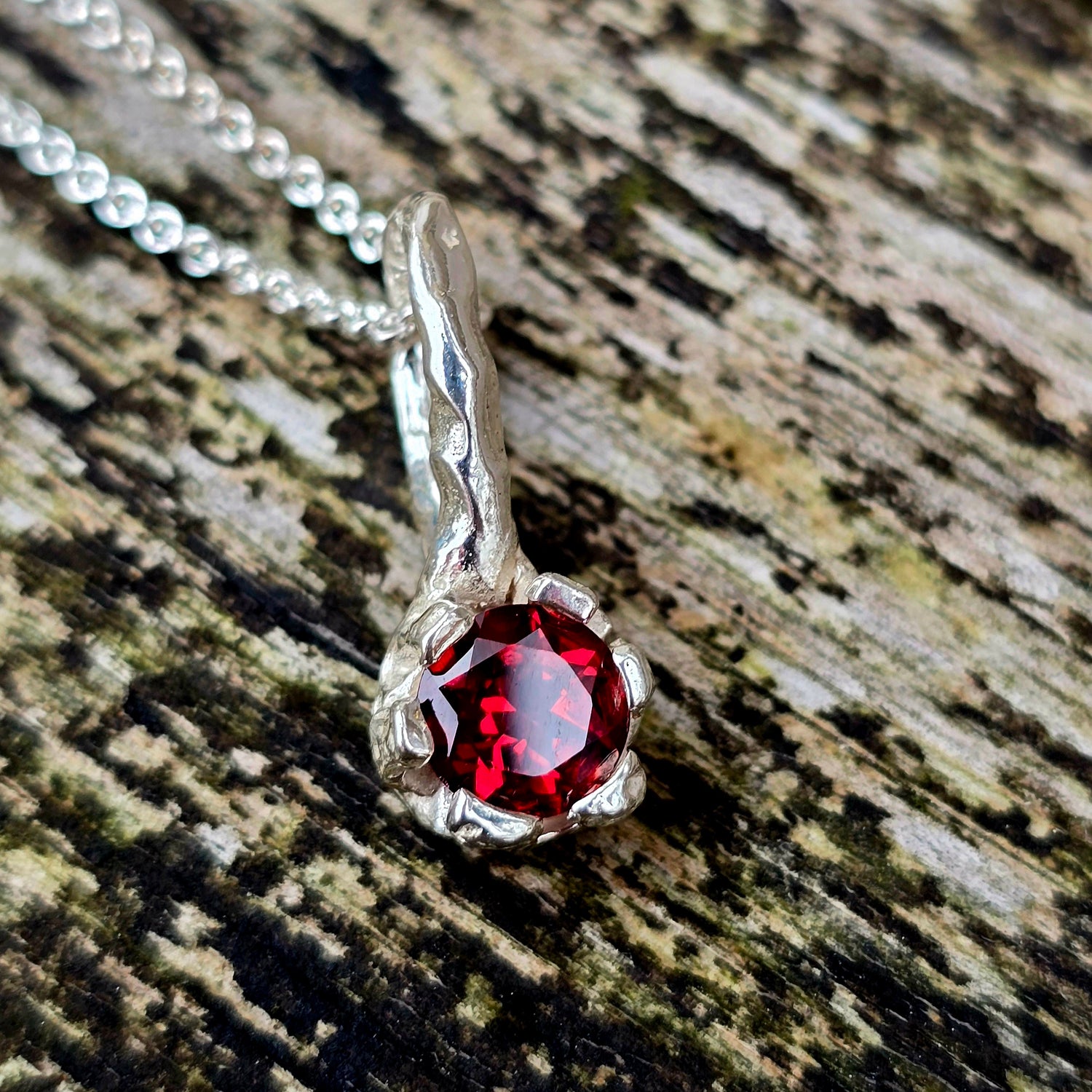 Granat-Anhänger aus Silber, handgefertigt mit organischer Krappenfassung. Der runde rote Edelstein ist ein Granat – Geburtsstein des Monats Januar. Die geschwungene Öse erinnert an Naturformen. Unikat-Schmuck für Liebhaber naturinspirierter Designs und ausdrucksstarker Edelsteine.